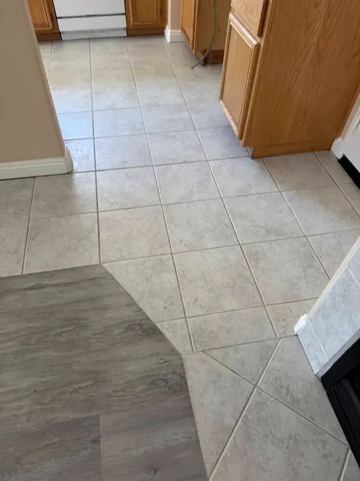 A close-up view showing the clean transition between grey square ceramic kitchen tile and dark wood-grain LVP flooring in a Wildomar, CA home, emphasizing deep grout cleaning