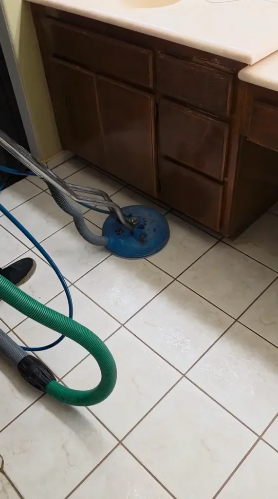 Heavily stained dark grout lines and trapped soil on square floor tiles near a baseboard